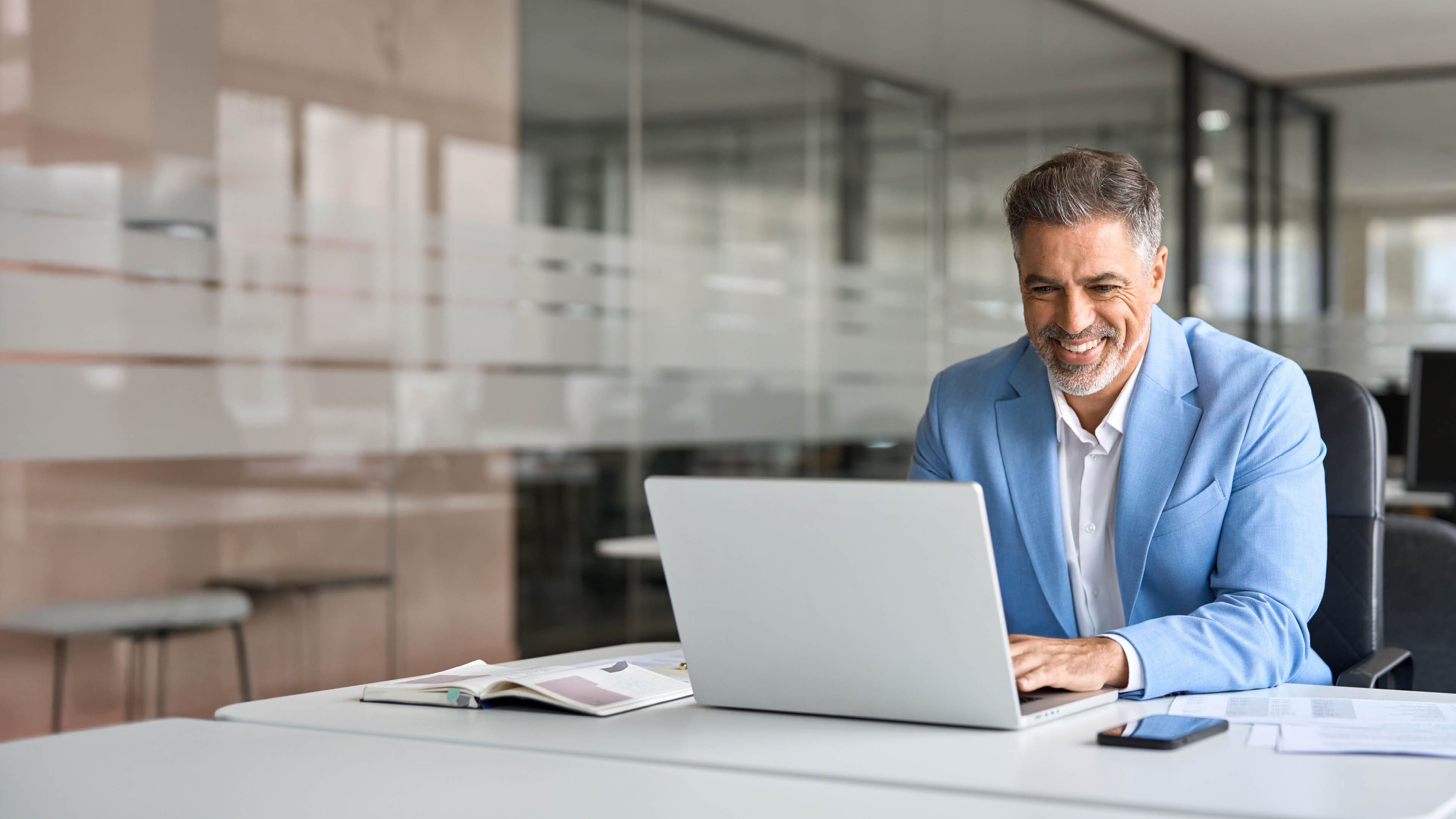 Happy senior 50 years old professional business man wearing suit using computer sitting at desk. Busy smiling middle aged businessman executive investor bank manager working on computer in office.