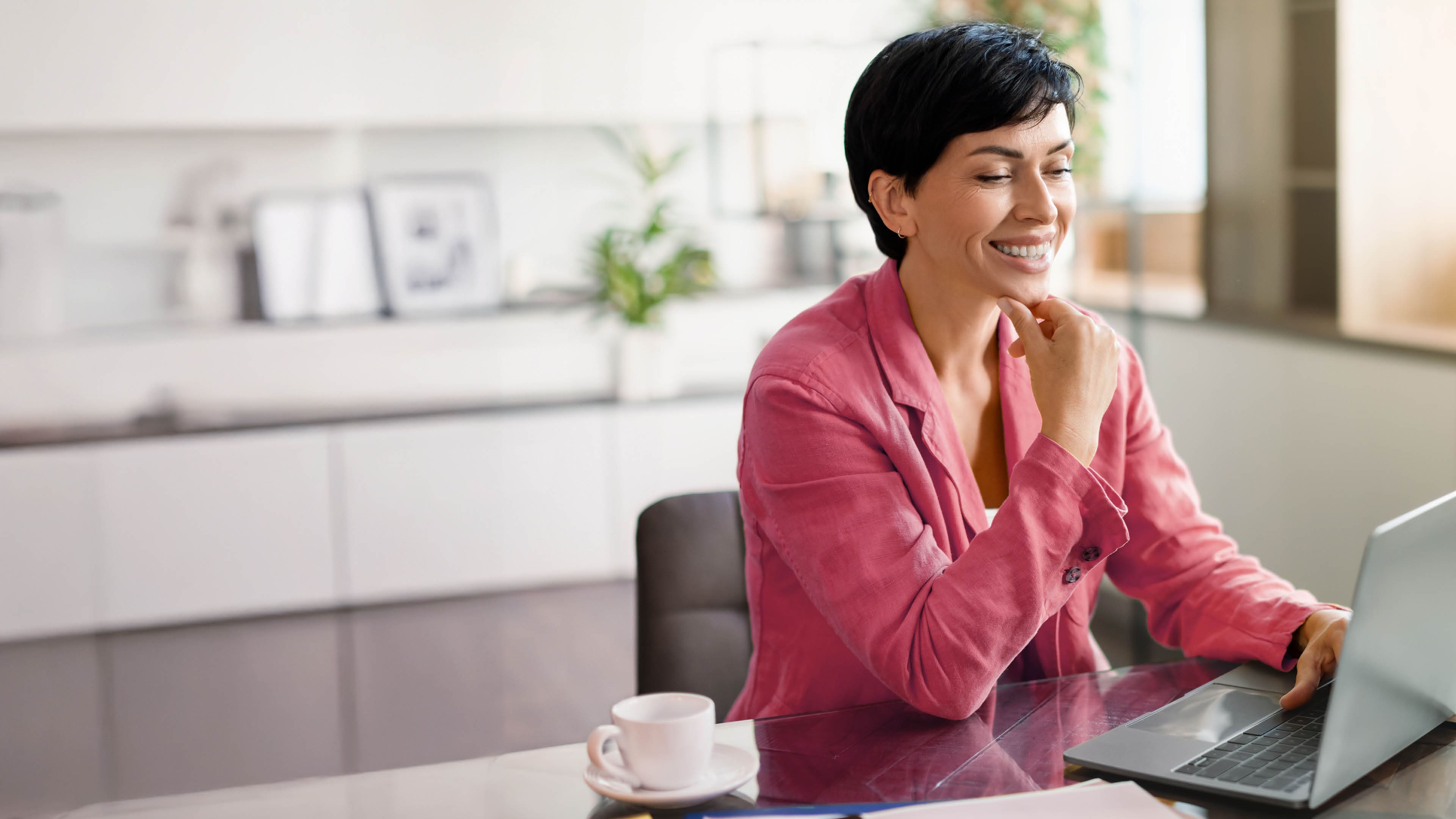 Smiling middle aged European businesswoman typing on laptop computer, browsing professional website, sitting at office table indoors. Modern digital business and online entrepreneurship